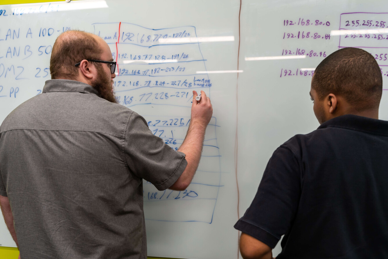Two bridge Academy students working together and solving complex math problems on a white board.