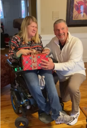 Kylie Moore with her supervisor at Bobby Dodd Institute, Jerry Sutton. Kylie is in her wheelchair. Jerry is kneeling next to her and giving her a Christmas present. 
