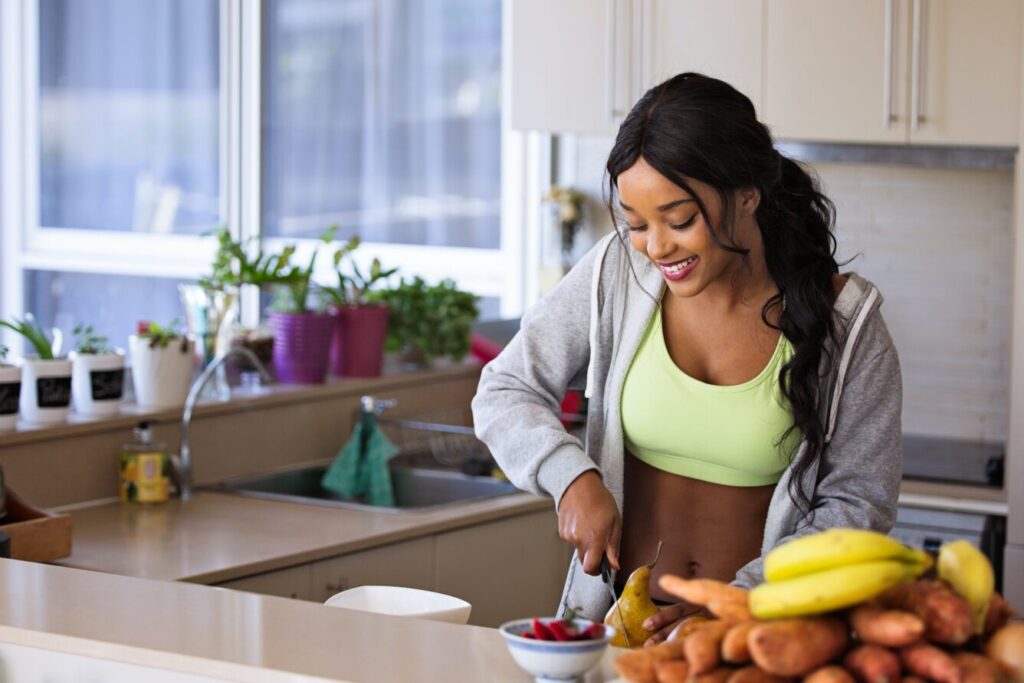 Young woman in a workout outfit making a fruit salad in a kitchen.