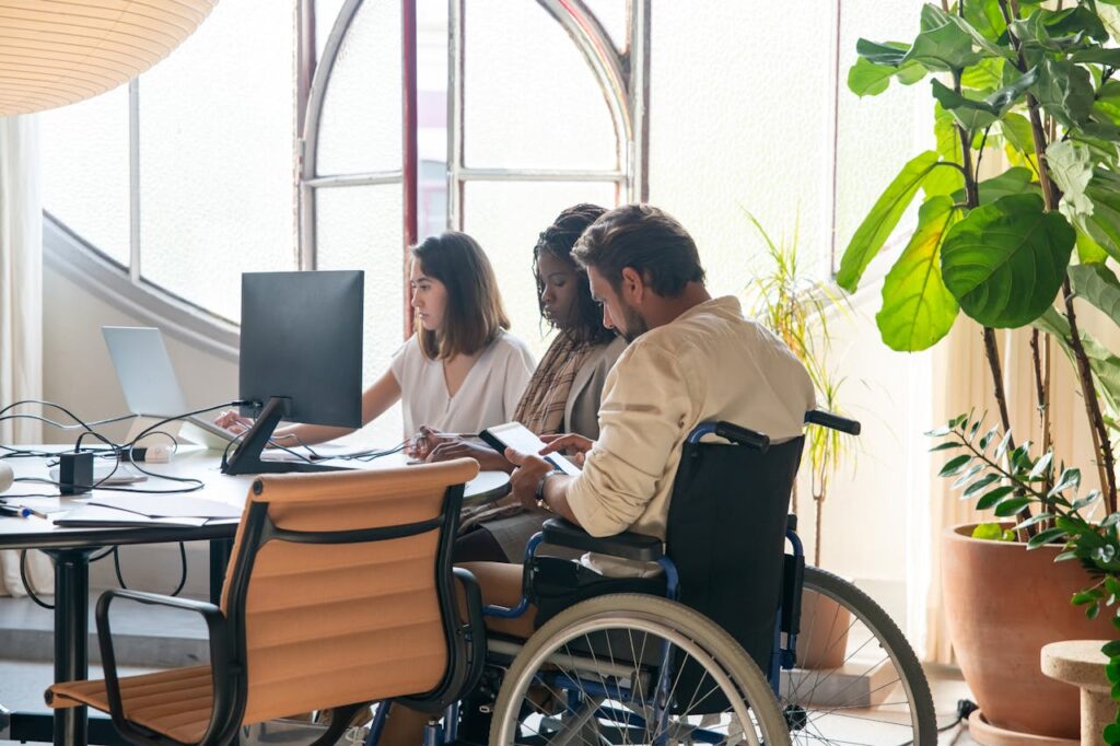 Three people working at at desk. One of them is in a wheelchair.