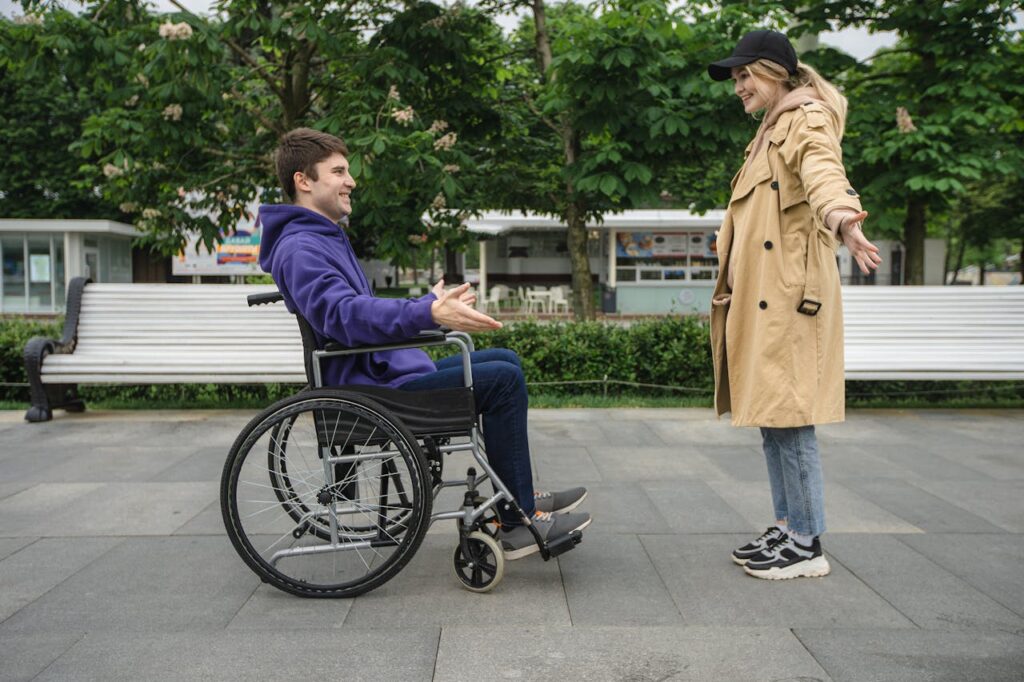 A man in a wheelchair cheerfully greets a girl. Both are with open arms preparing for hug.