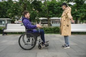 A man in a wheelchair cheerfully greets a girl. Both are with open arms preparing for hug.
