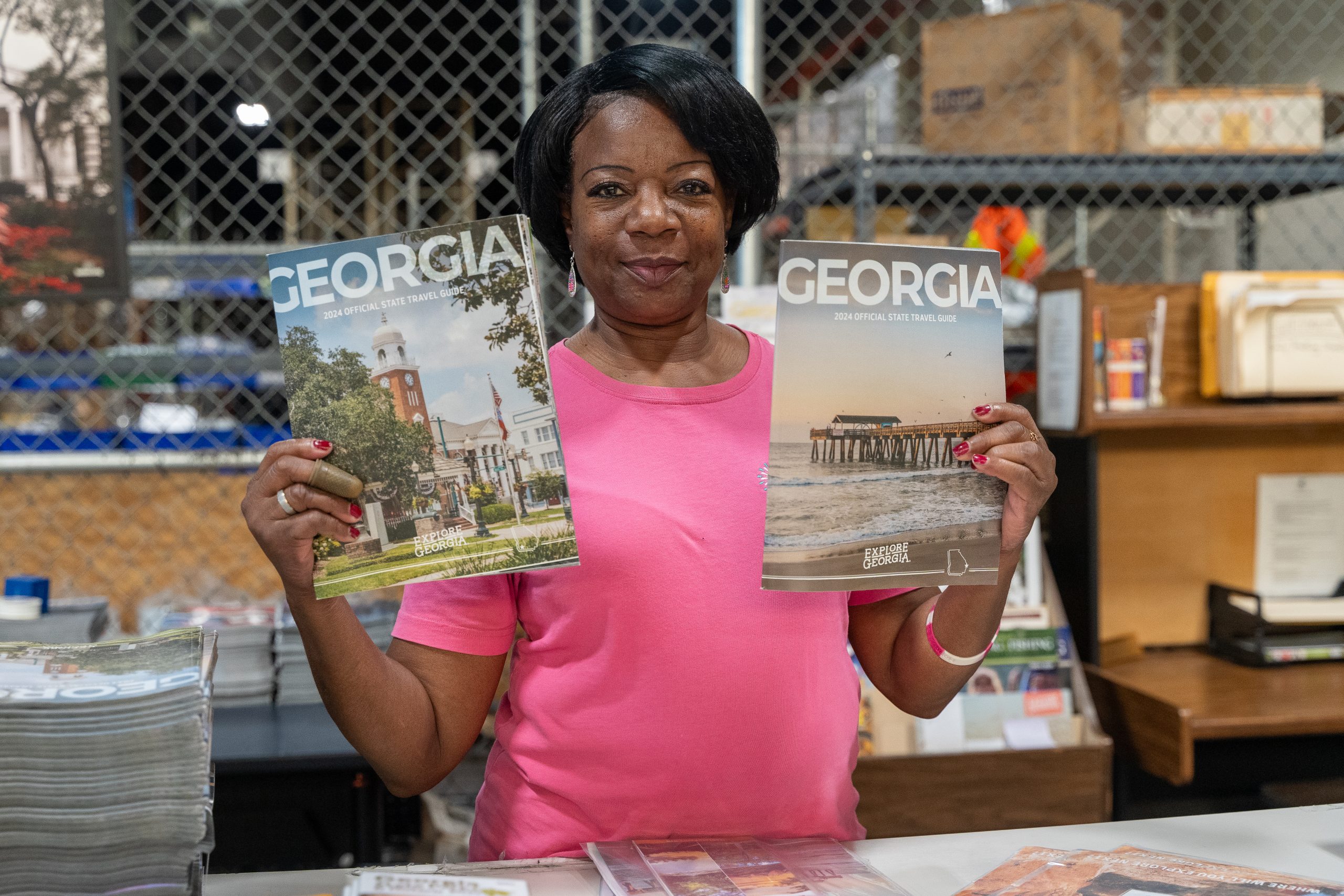 Angela, a BDI employee, working on the Georgia Tourism contract. She is holding the Georgia 2024 Official State Travel Guide that is being packaged in the BDI's facility and then distributed to various locations across the state.