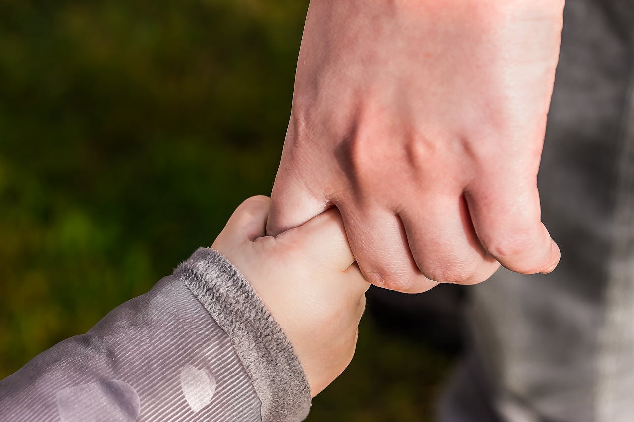 Adult and child holding hands outdoors.