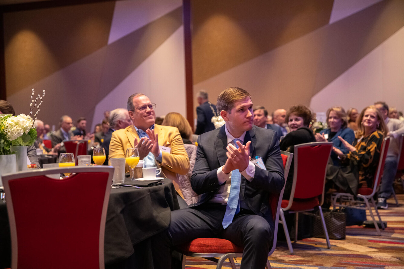 Attendees of the 2024 Breakfast with Champions event applauding an unseen speaker on stage.