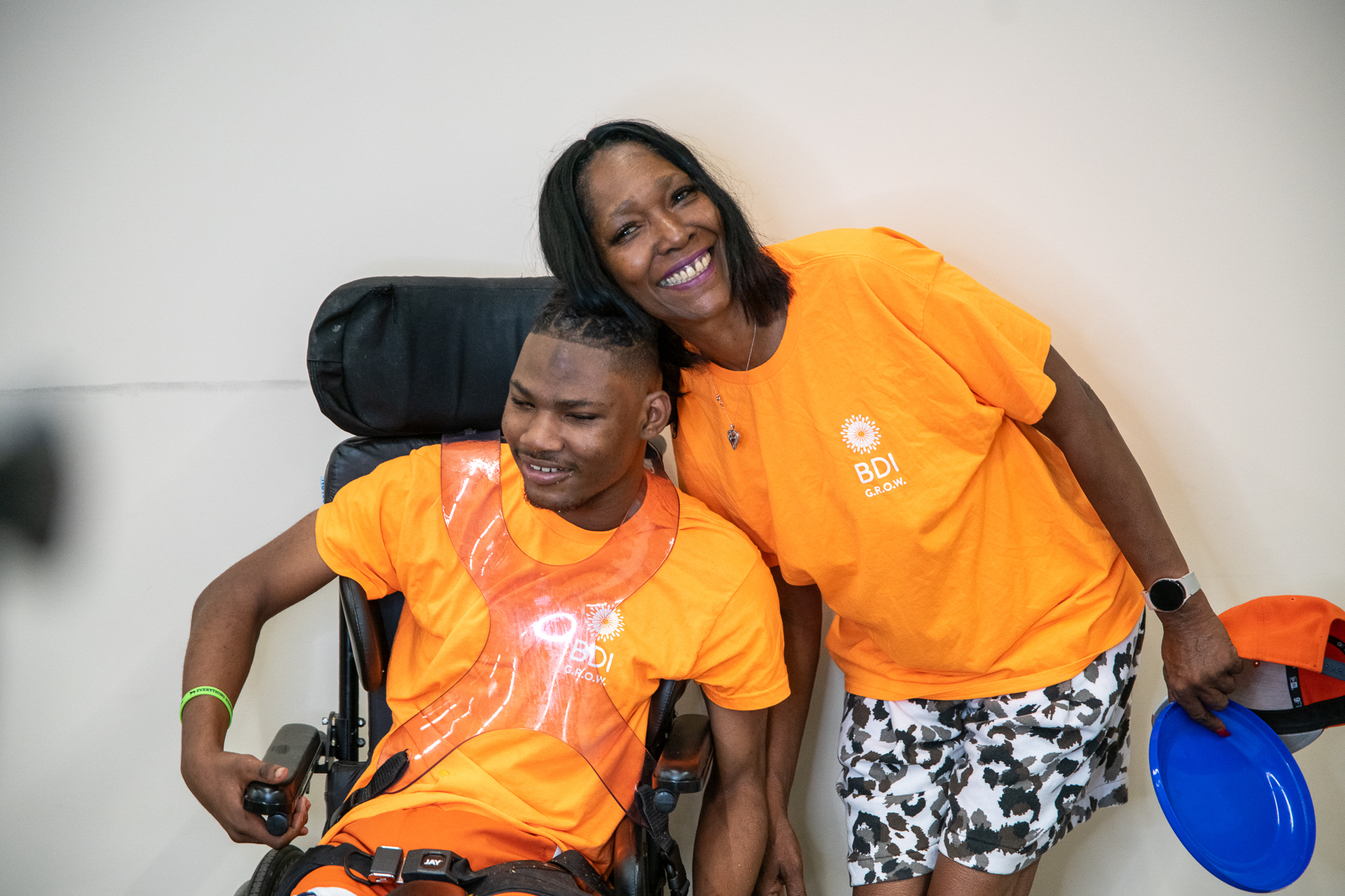 A BDI GROW participant, a wheelchair user, with his mom, both wearing orange GROW t-shirs, both smiling
