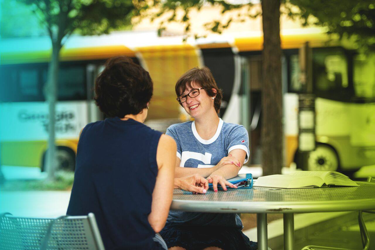 Kendall, a BDI service participant, sitting at a table with her mom, and smiling.