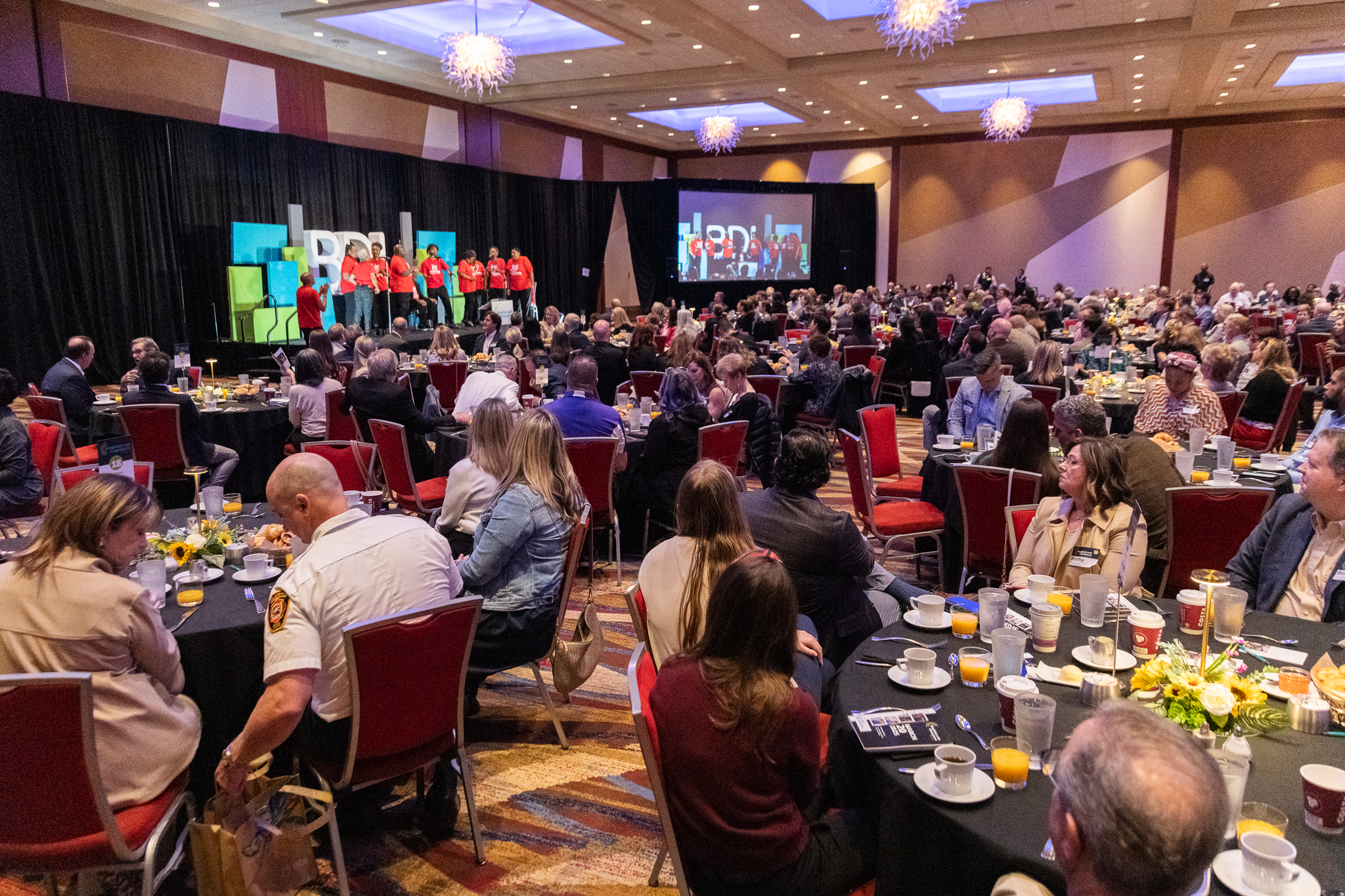Breakfast with Champions 2025 attendees and the SHOWAbility inclusive chorus performing on stage.