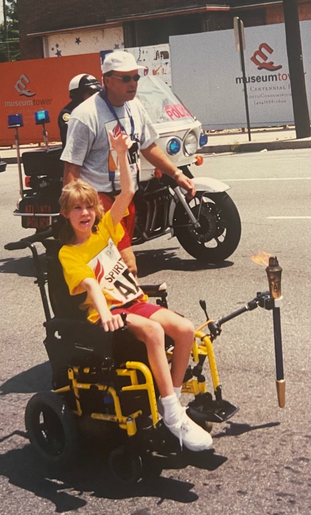Kylie Moore at the Spirit of the ADA Torch rally carrying the torch accompanied by her dad. 